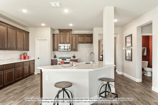 kitchen with visible vents, wood finished floors, stainless steel appliances, a kitchen bar, and a sink