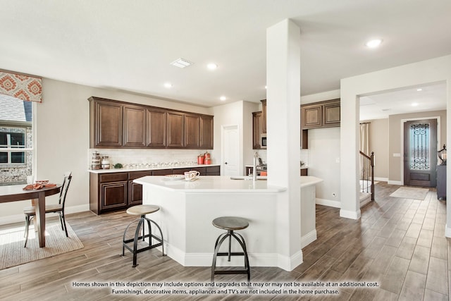 kitchen with wood tiled floor, a kitchen bar, decorative backsplash, and light countertops