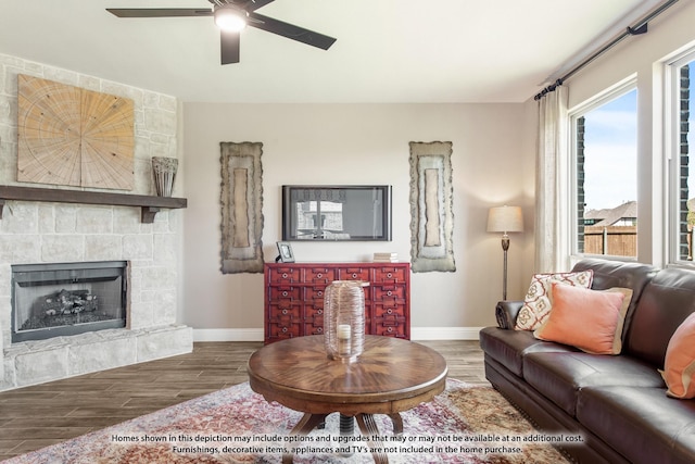 living room featuring ceiling fan, a fireplace, baseboards, and wood finished floors