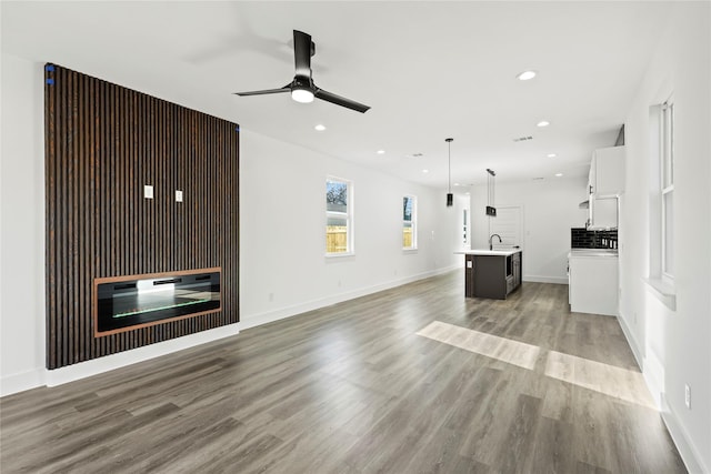 unfurnished living room featuring baseboards, light wood finished floors, a sink, and recessed lighting