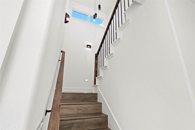 staircase featuring wood finished floors, a towering ceiling, and baseboards