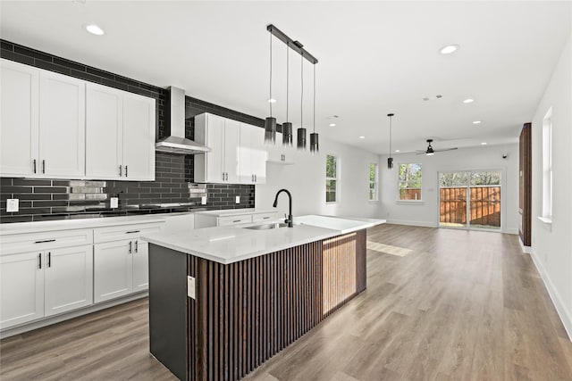 kitchen with light wood finished floors, tasteful backsplash, white cabinetry, a sink, and wall chimney range hood