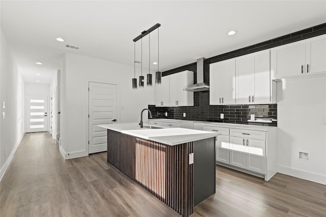 kitchen featuring wall chimney range hood, visible vents, backsplash, and a sink