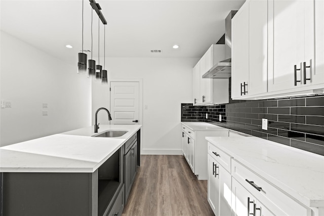 kitchen with backsplash, a sink, a kitchen island with sink, and light stone countertops