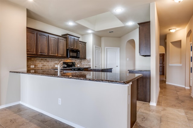 kitchen featuring dark brown cabinetry, a peninsula, backsplash, black appliances, and dark stone countertops