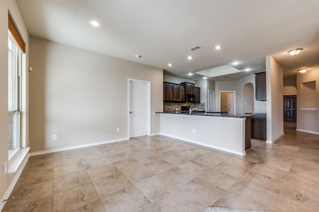 kitchen with visible vents, arched walkways, dark countertops, black microwave, and backsplash