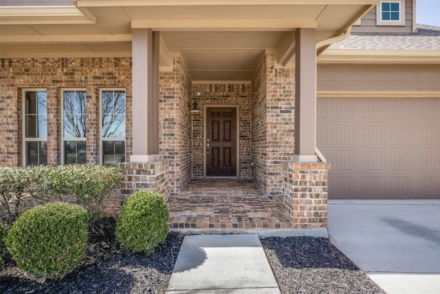 entrance to property featuring an attached garage, a shingled roof, and brick siding