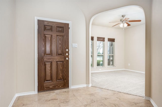 entryway with baseboards, arched walkways, a ceiling fan, and light colored carpet