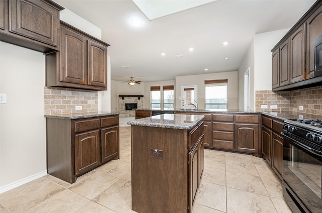 kitchen featuring a peninsula, a fireplace, black range with gas stovetop, backsplash, and dark stone counters