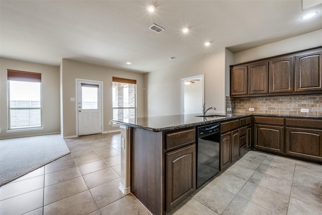 kitchen with black dishwasher, decorative backsplash, a sink, dark stone counters, and a peninsula