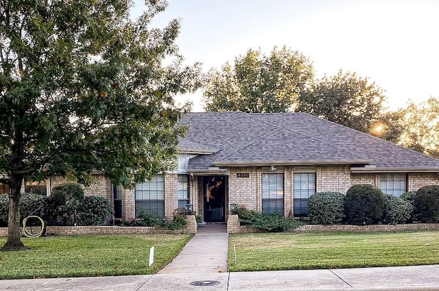 view of front of house featuring brick siding, roof with shingles, and a front lawn