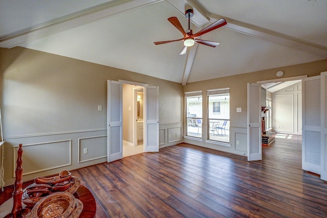 unfurnished living room featuring a ceiling fan, lofted ceiling with beams, dark wood-style floors, wainscoting, and a decorative wall