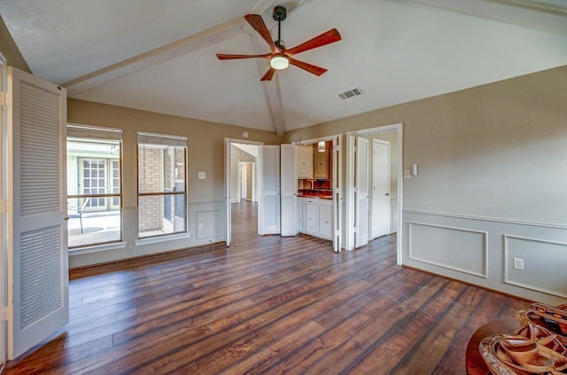 spare room featuring visible vents, lofted ceiling with beams, wainscoting, ceiling fan, and dark wood-style flooring