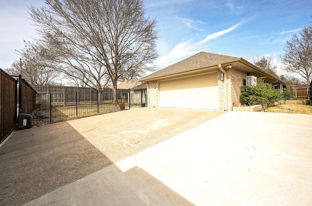 view of side of property with brick siding, driveway, a garage, and fence