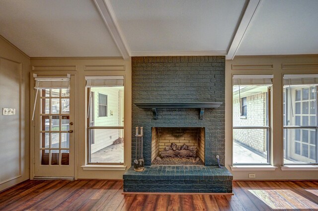 unfurnished living room featuring beam ceiling, wood-type flooring, a brick fireplace, and a decorative wall