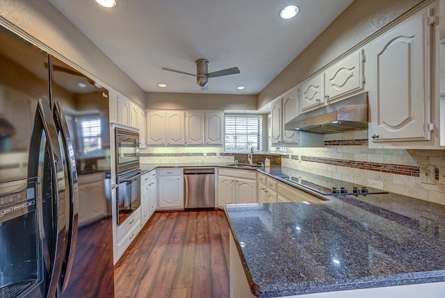 kitchen with black appliances, under cabinet range hood, backsplash, dark wood finished floors, and a peninsula