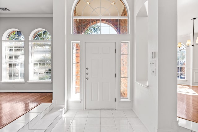 foyer entrance with a chandelier, ornamental molding, visible vents, and a healthy amount of sunlight