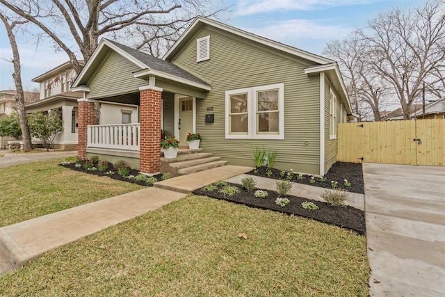 view of front of property featuring brick siding, covered porch, a gate, fence, and a front yard