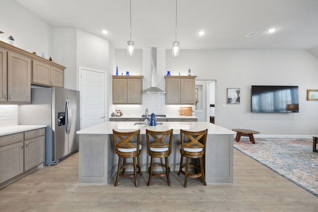 kitchen with stainless steel appliances, light countertops, an island with sink, light wood-type flooring, and wall chimney exhaust hood