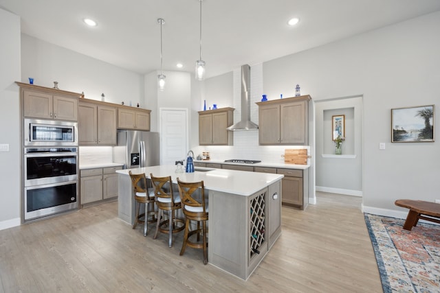 kitchen featuring light countertops, appliances with stainless steel finishes, a kitchen island with sink, wall chimney range hood, and a kitchen bar