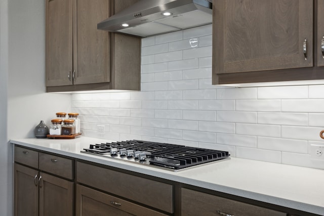 kitchen featuring light countertops, stainless steel gas stovetop, decorative backsplash, dark brown cabinets, and wall chimney exhaust hood