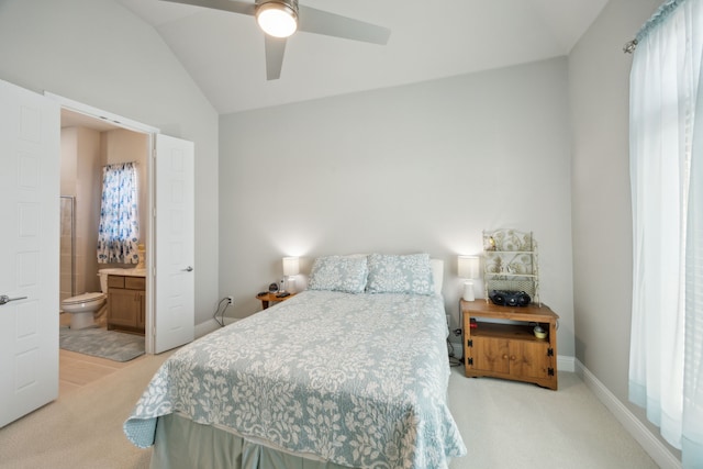 bedroom with baseboards, light colored carpet, ceiling fan, ensuite bath, and vaulted ceiling