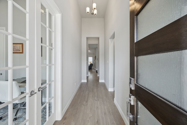 corridor with an inviting chandelier, baseboards, wood finished floors, and french doors