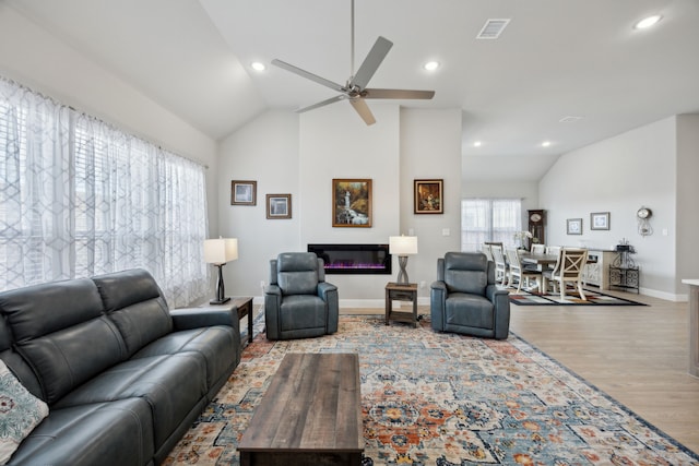 living area featuring a glass covered fireplace, visible vents, vaulted ceiling, and wood finished floors