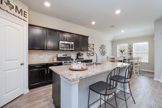 kitchen with light wood-style flooring, stainless steel appliances, a sink, a kitchen breakfast bar, and decorative backsplash