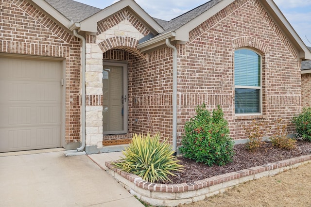 property entrance with an attached garage, a shingled roof, and brick siding