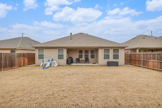 rear view of property with roof with shingles, a patio area, a fenced backyard, and a lawn