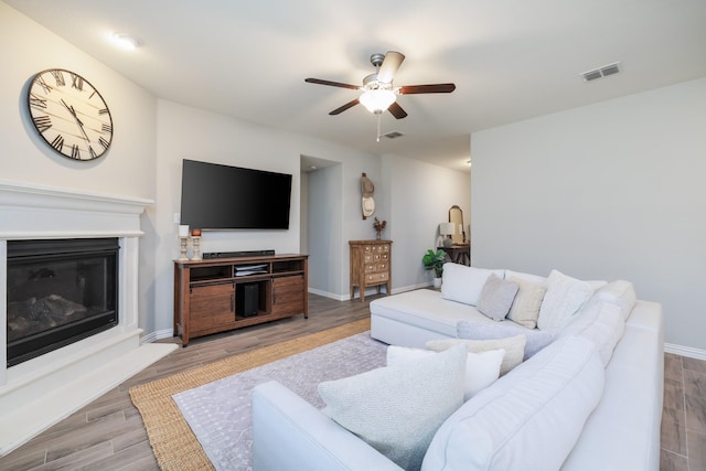 living area with visible vents, light wood-style floors, a glass covered fireplace, ceiling fan, and baseboards