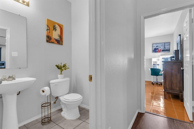 half bathroom with tile patterned flooring, baseboards, a sink, and toilet