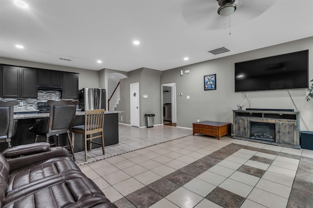 living room featuring recessed lighting, visible vents, a glass covered fireplace, stairs, and light tile patterned flooring