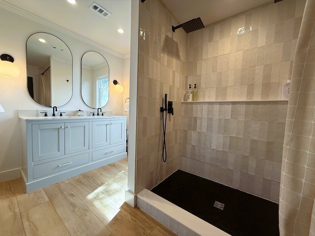 bathroom featuring double vanity, visible vents, wood finished floors, walk in shower, and crown molding