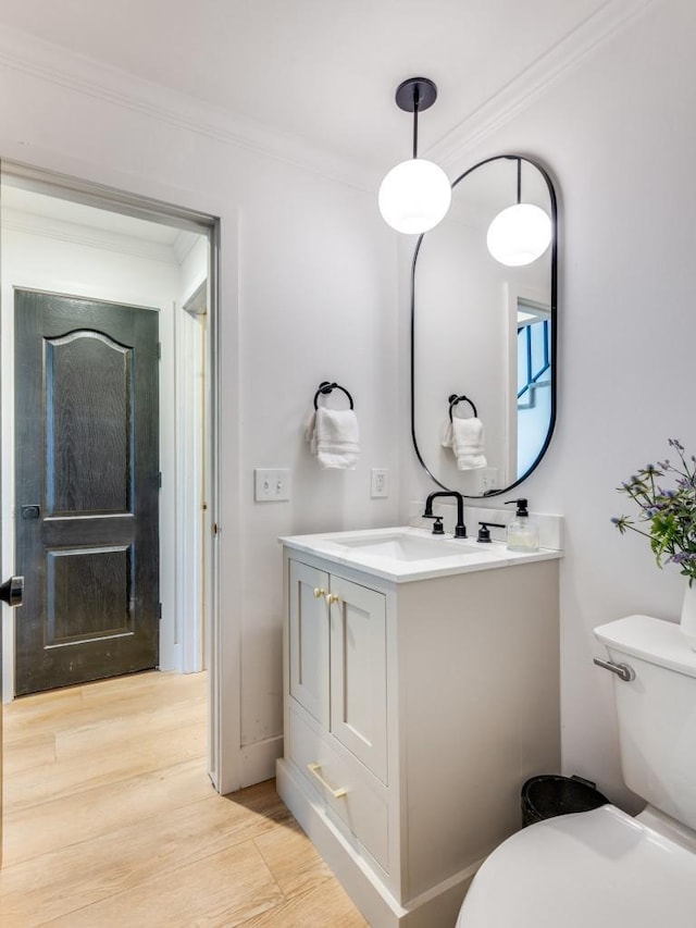 bathroom with toilet, wood finished floors, vanity, and crown molding