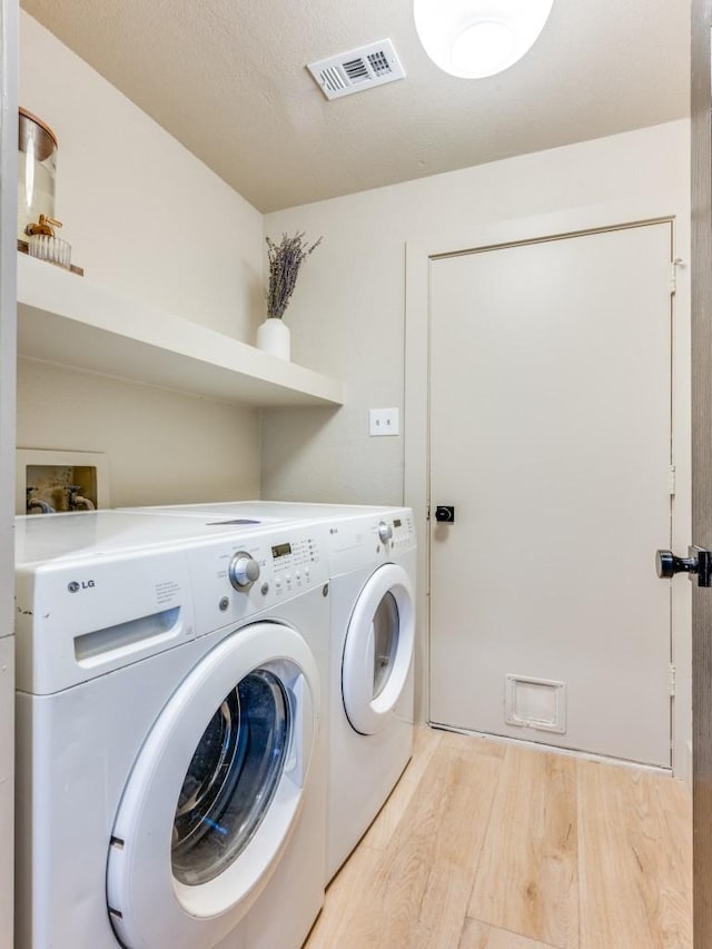 laundry area with a textured ceiling, washing machine and dryer, laundry area, visible vents, and light wood-type flooring