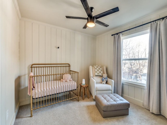 carpeted bedroom featuring ornamental molding, ceiling fan, and a crib