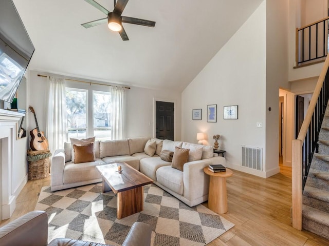 living area with visible vents, ceiling fan, high vaulted ceiling, light wood-type flooring, and stairs