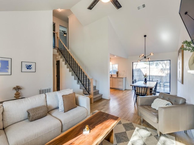 living area with light wood-style flooring, visible vents, stairway, and ceiling fan with notable chandelier