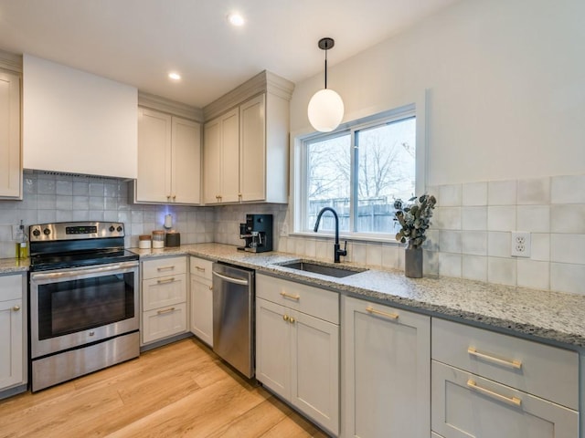 kitchen featuring light wood finished floors, tasteful backsplash, appliances with stainless steel finishes, and a sink