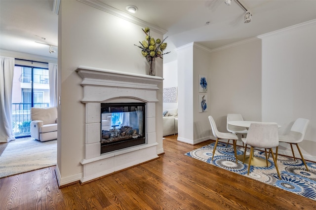 dining room with track lighting, wood finished floors, a multi sided fireplace, crown molding, and baseboards