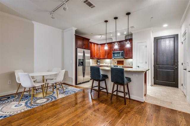 kitchen with visible vents, ornamental molding, appliances with stainless steel finishes, light wood finished floors, and decorative backsplash