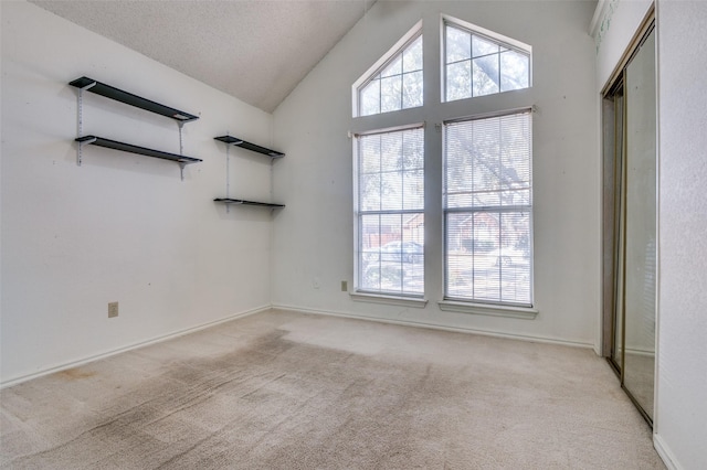 empty room with high vaulted ceiling, light colored carpet, a textured ceiling, and baseboards