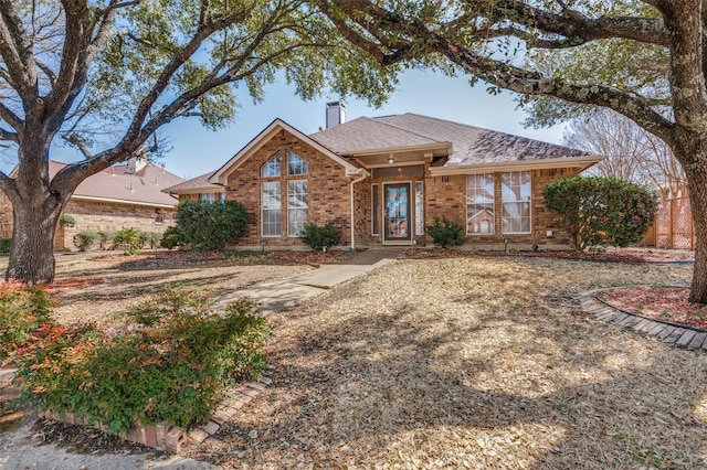 ranch-style house featuring a shingled roof, brick siding, and a chimney