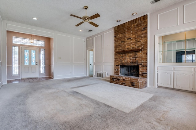 unfurnished living room with visible vents, light colored carpet, a textured ceiling, a fireplace, and a decorative wall