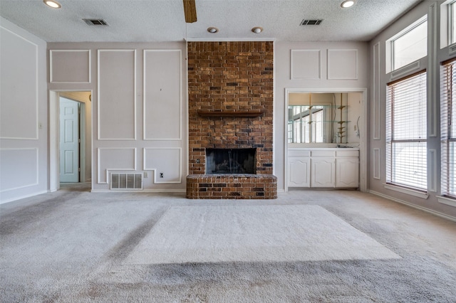 unfurnished living room featuring a brick fireplace, light colored carpet, visible vents, and a decorative wall