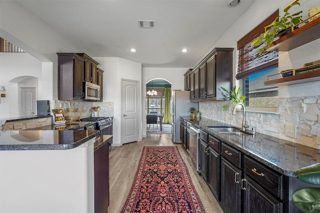 kitchen featuring arched walkways, open shelves, visible vents, appliances with stainless steel finishes, and a sink