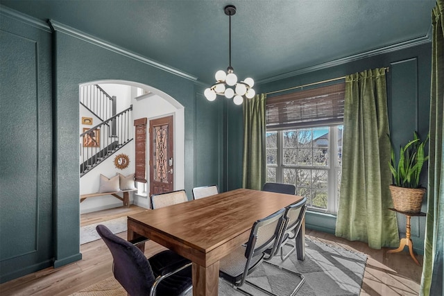 dining room featuring arched walkways, light wood-style flooring, a notable chandelier, stairway, and crown molding