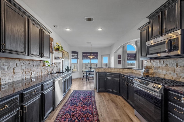 kitchen featuring visible vents, dark stone countertops, stainless steel appliances, light wood-style floors, and a sink